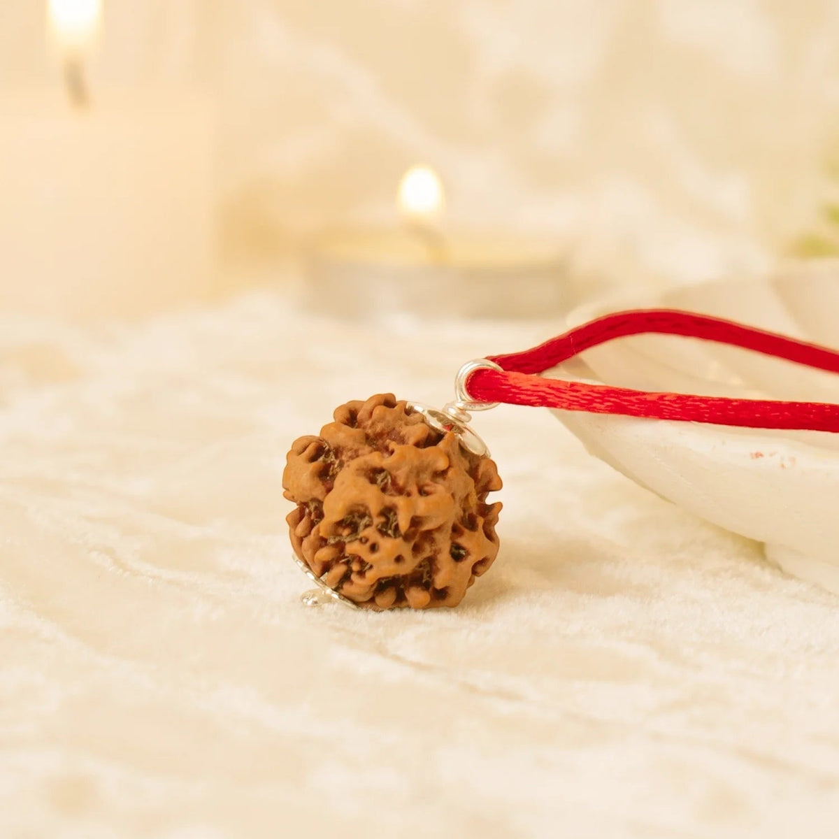 VASTUKOSHA Nepal origin 0 Mukhi Nirakar Rudraksha pendant on a red cord, set against a soft, candlelit background.