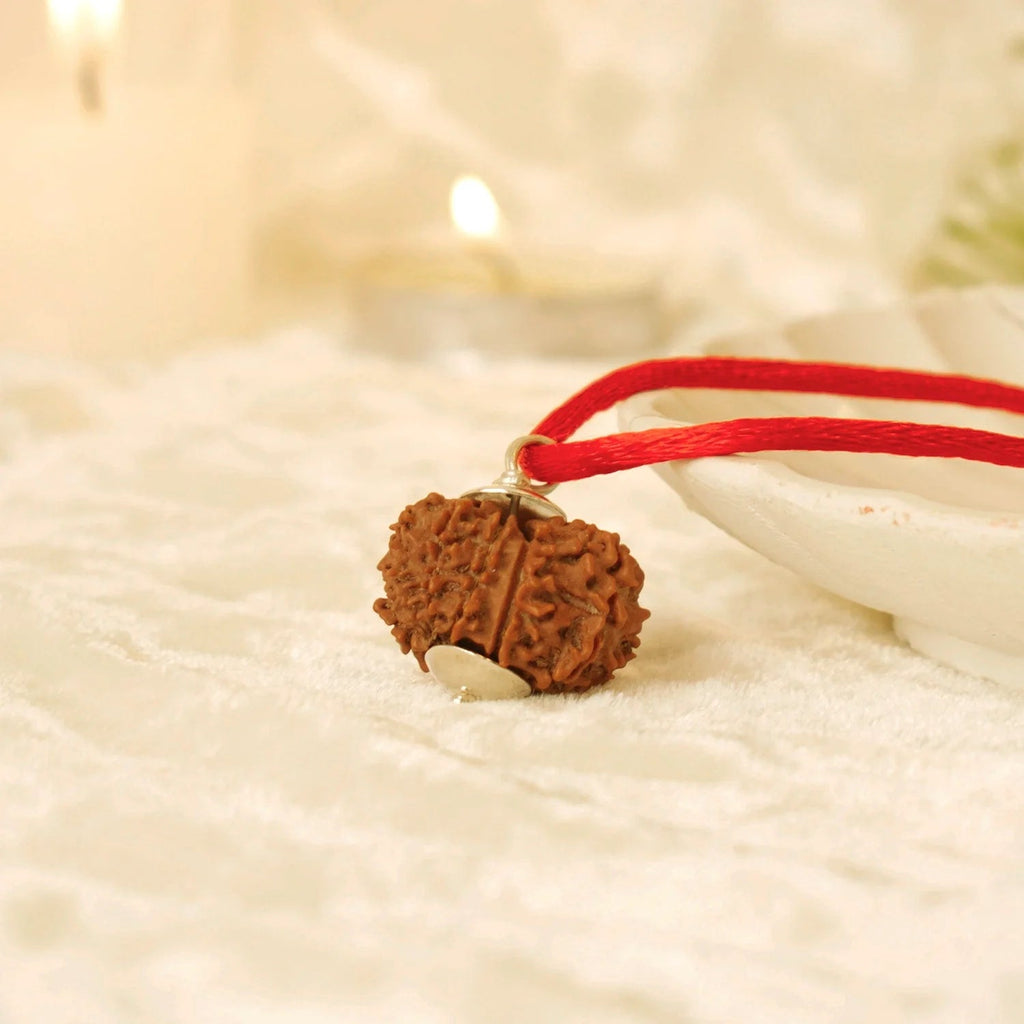 VASTUKOSHA 12 Mukhi Nepal Rudraksha bead pendant on a red thread, resting on a white textured surface with candlelight.
