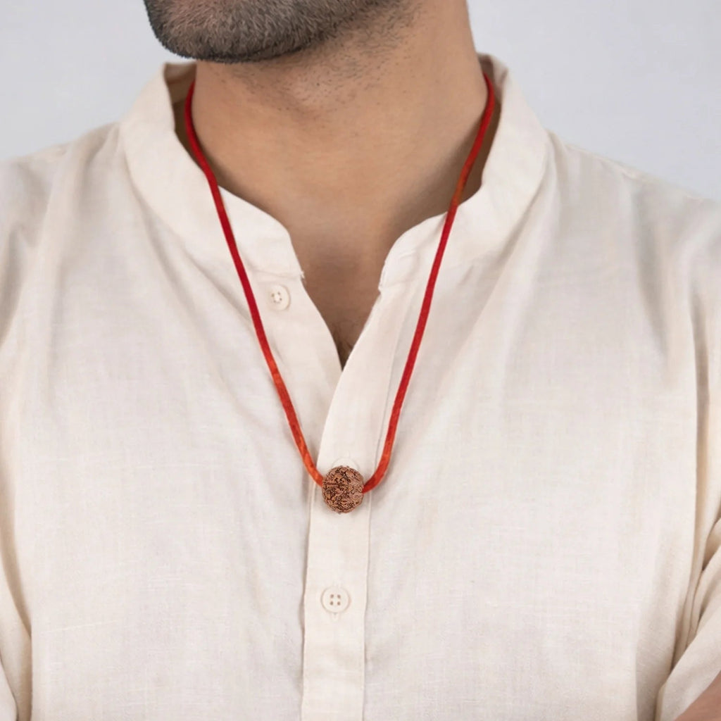 Man wearing a VASTUKOSHA 7 Mukhi Nepal origin Rudraksha bead on a simple red thread necklace against a white background.