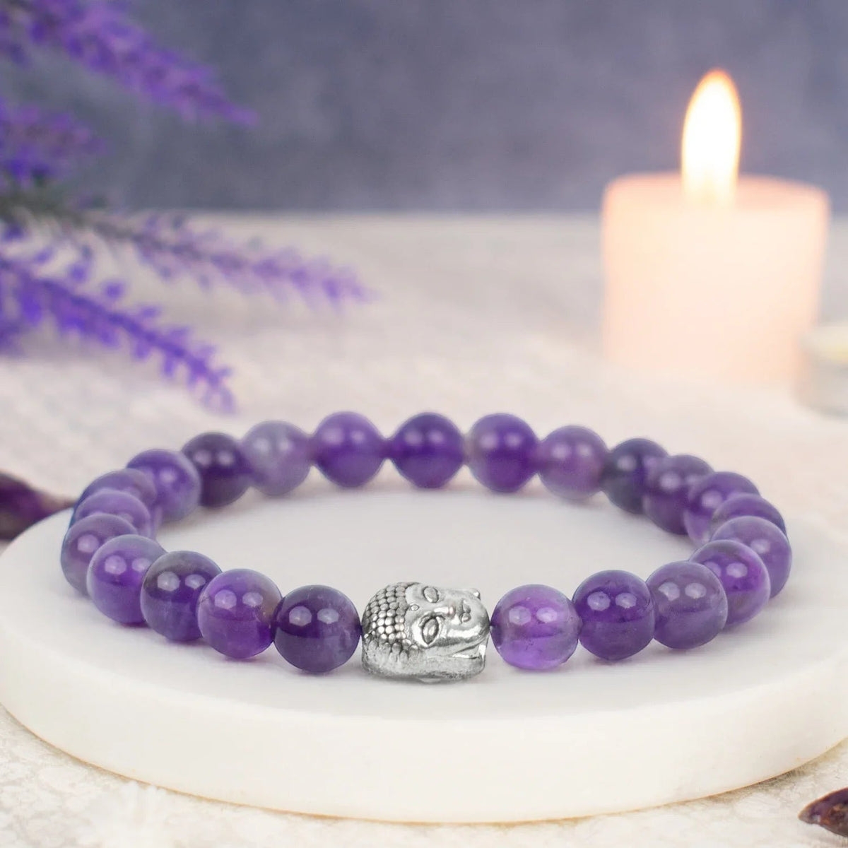 VASTUKOSHA 8mm natural purple amethyst bead bracelet with a silver-toned Buddha charm on a white stone display base.