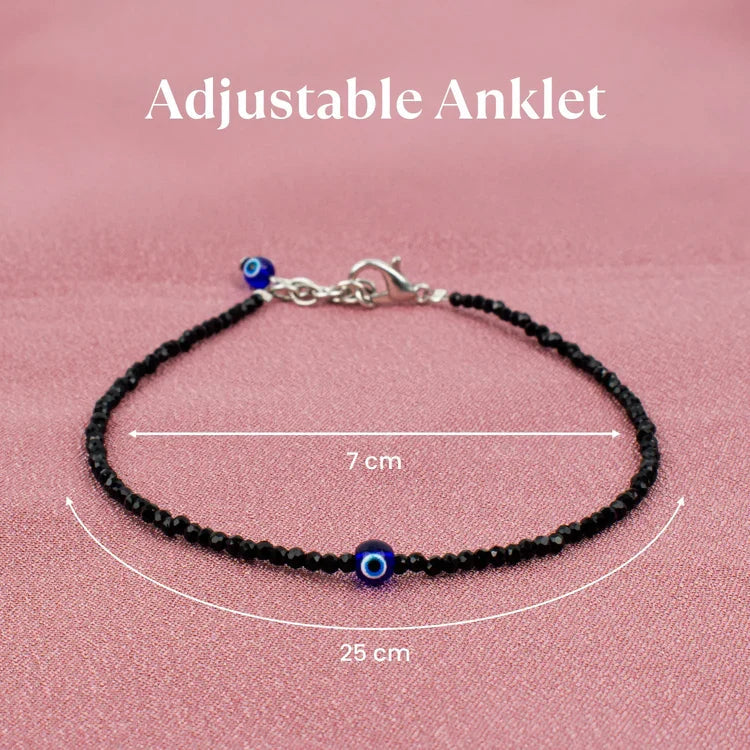 VASTUKOSHA black tourmaline beaded anklet with a blue evil eye charm and adjustable silver-tone clasp on pink fabric.