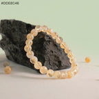 VASTUKOSHA citrine beaded bracelet with warm yellow translucent stones, displayed against a dark textured rock.
