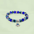 VASTUKOSHA Evil Eye Hamsa bracelet with blue glass beads and a silver-toned Hamsa hand charm on a light green background