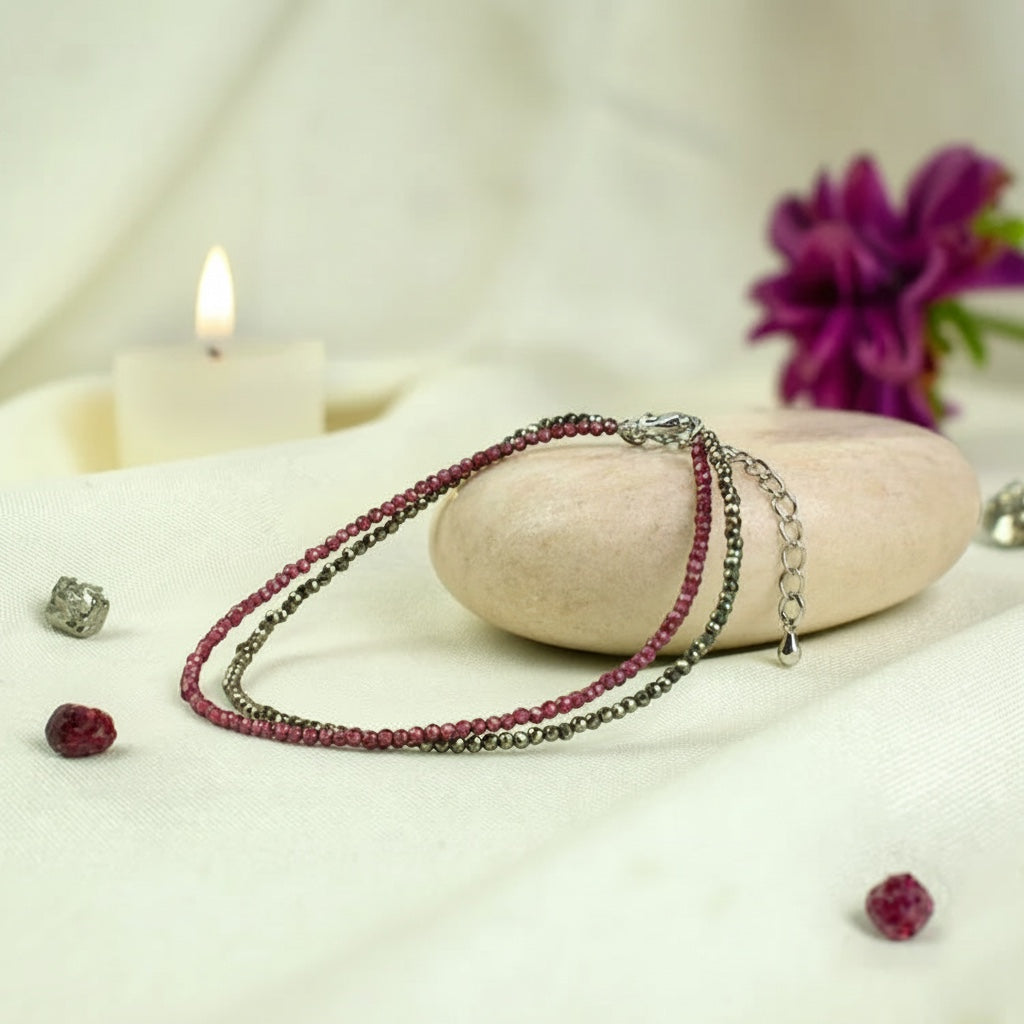 VASTUKOSHA Love and Money anklet featuring garnet and pyrite beads resting on a raw selenite plate with a candle.
