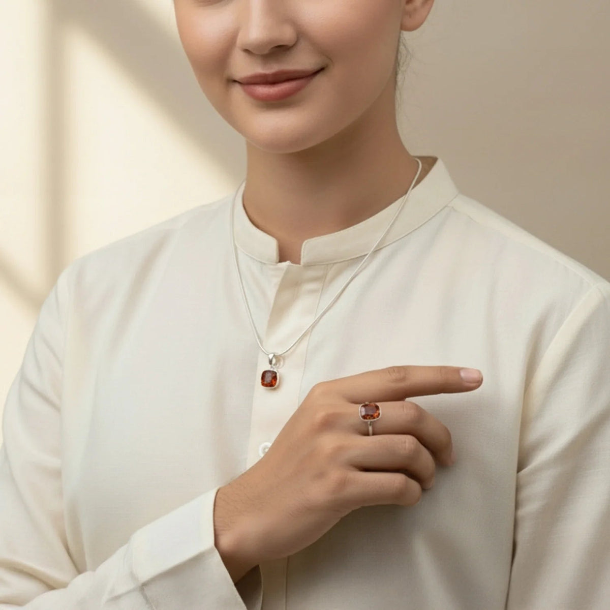 Woman wearing a VASTUKOSHA natural hessonite garnet pendant and matching ring set in silver, featuring warm honey-brown tones.