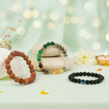 VASTUKOSHA Maha Dhan Yog Combo featuring a 5 Mukhi Rudraksha bracelet, a multi-stone prosperity bracelet, and an Evil Eye black obsidian bracelet on a light green surface.