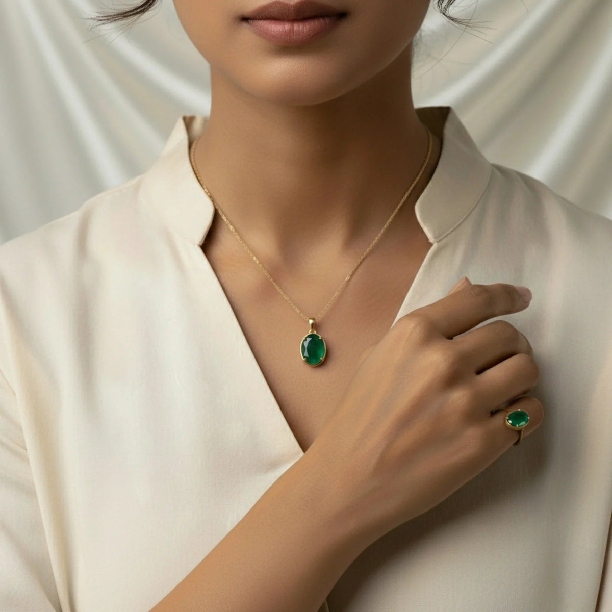 VASTUKOSHA natural emerald pendant and ring set in gold, worn by a woman in a cream blouse.