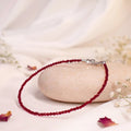 VASTUKOSHA natural garnet beaded anklet with delicate red stones on a smooth stone surface with white flowers