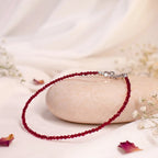 VASTUKOSHA natural garnet beaded anklet with delicate red stones on a smooth stone surface with white flowers