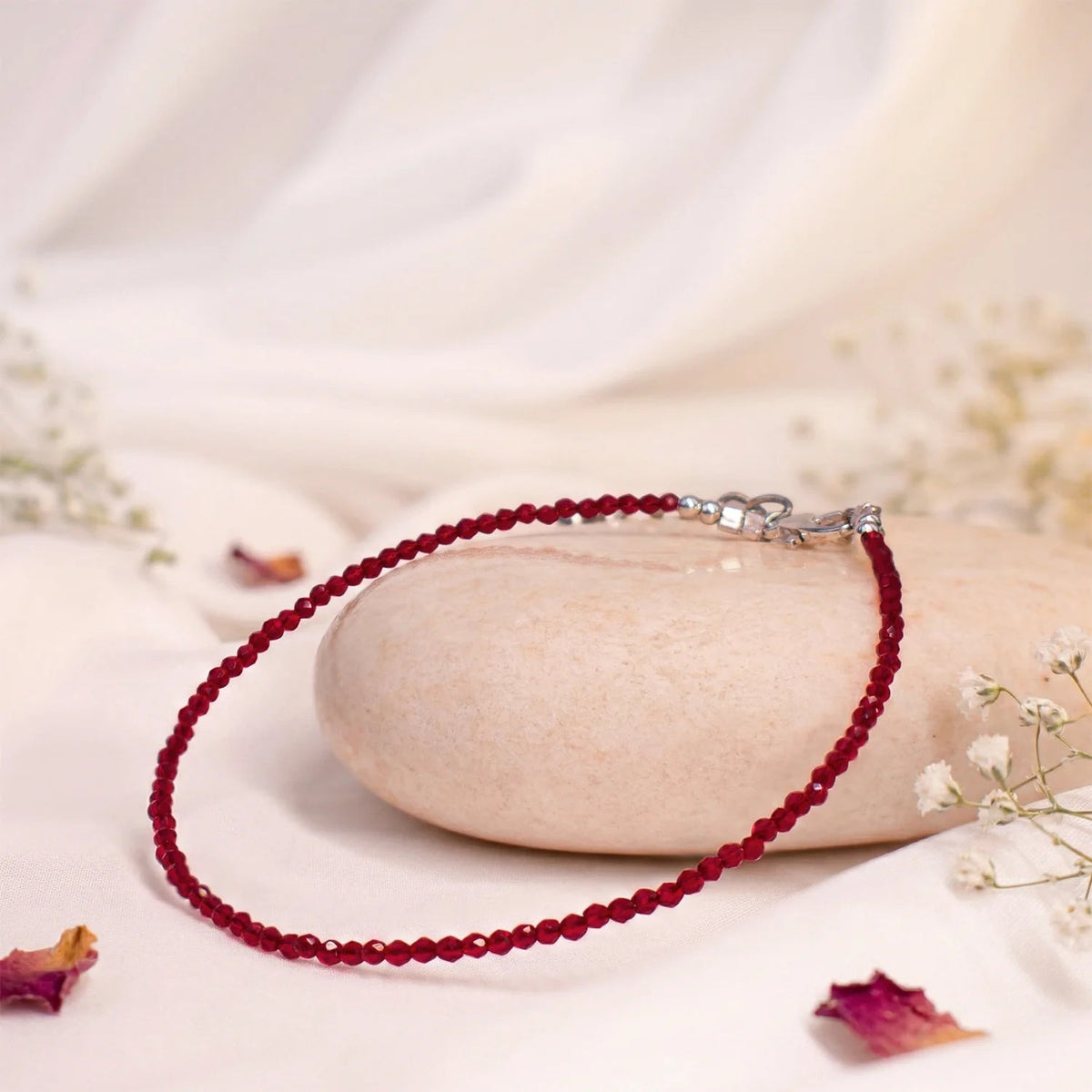 VASTUKOSHA natural garnet beaded anklet with delicate red stones on a smooth stone surface with white flowers