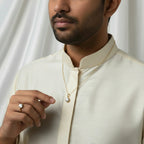 A man wearing a VASTUKOSHA natural zircon ring and pendant set in gold, styled with a traditional cream-colored kurta.