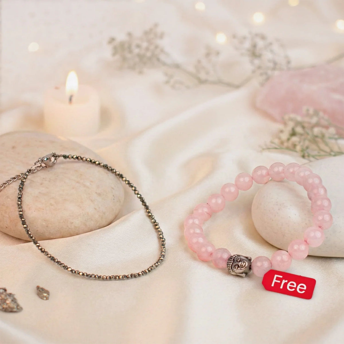 VASTUKOSHA pyrite anklet and rose quartz Buddha bracelet set on a soft fabric background with a candle.