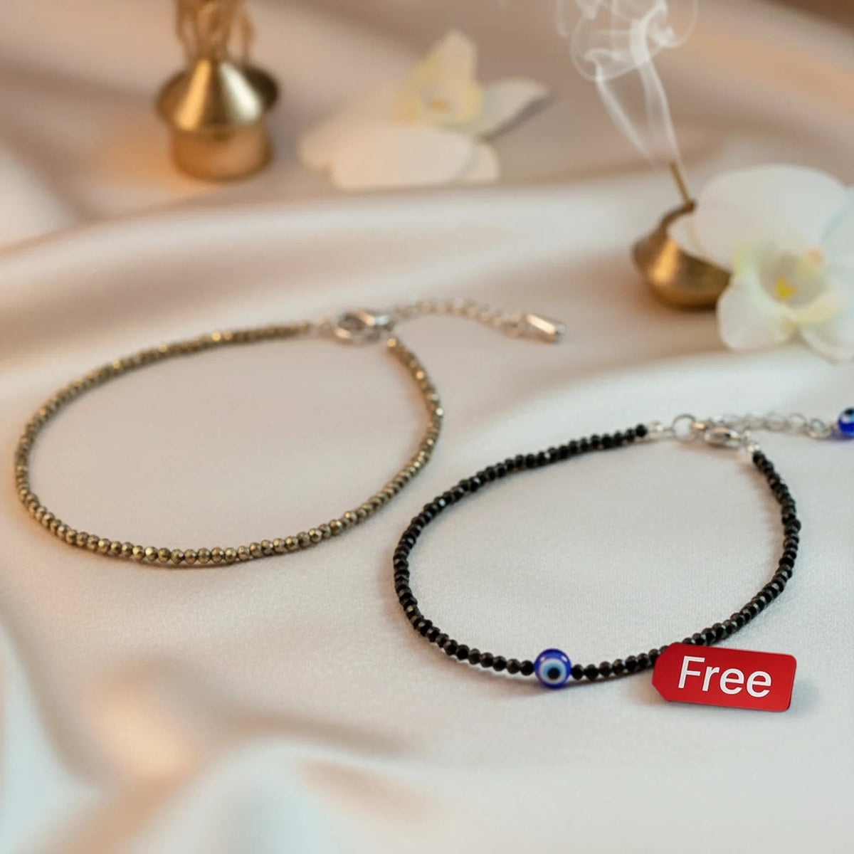 VASTUKOSHA pyrite and black tourmaline anklet set with evil eye charm on a soft fabric background