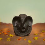 VASTUKOSHA Pyrite Ganesha idol with a metallic finish, displayed on a table with marigold flowers and lit candles.