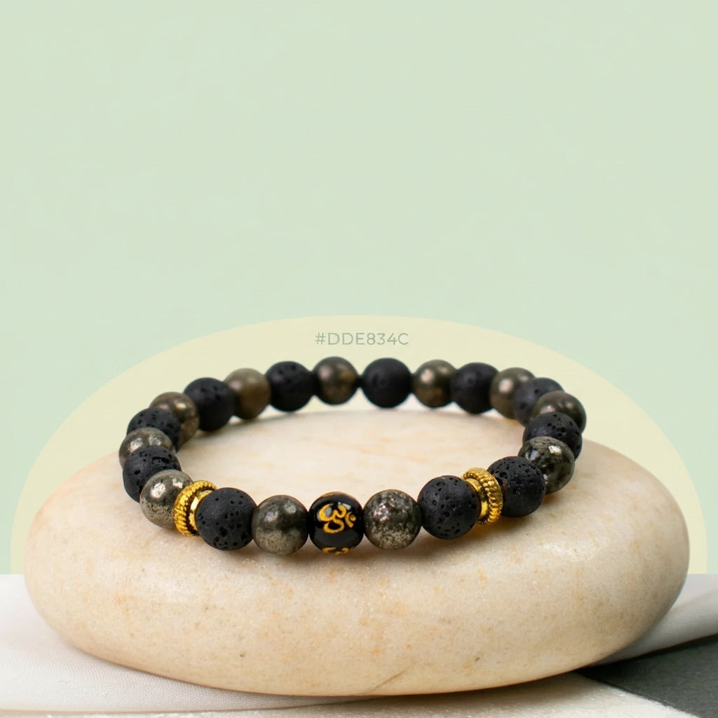 VASTUKOSHA Wealth OM bracelet featuring raw pyrite, black lava beads, and a central gold Om symbol on a stone base.