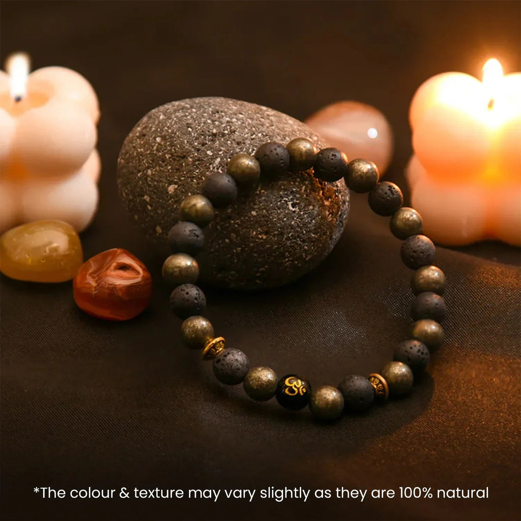 VASTUKOSHA wealth OM pyrite bracelet with lava beads and sacred Om symbol, displayed with candles and stones.