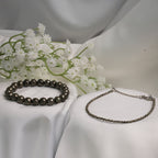 VASTUKOSHA raw pyrite bracelet and delicate pyrite anklet set displayed on white fabric with white flowers.