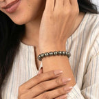 A person wearing a VASTUKOSHA raw pyrite beaded bracelet on their wrist, featuring metallic grey natural crystal beads.