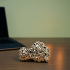 VASTUKOSHA energised raw pyrite cluster on a wooden desk with a laptop in the background for prosperity and Vastu.