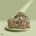 VASTUKOSHA raw pyrite stone with metallic luster on a green circular pedestal, symbolizing prosperity and abundance.