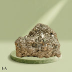 VASTUKOSHA raw pyrite stone with metallic luster on a green circular pedestal, symbolizing prosperity and abundance.
