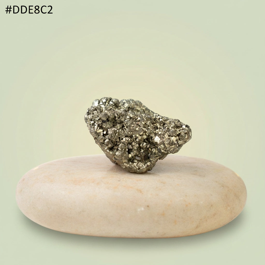 VASTUKOSHA raw metallic gold pyrite stone with natural texture resting on a smooth beige pebble for display