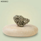 VASTUKOSHA raw metallic gold pyrite stone with natural texture resting on a smooth beige pebble for display