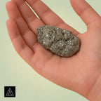 VASTUKOSHA raw pyrite stone with metallic luster held in a palm, symbolizing prosperity and grounding.