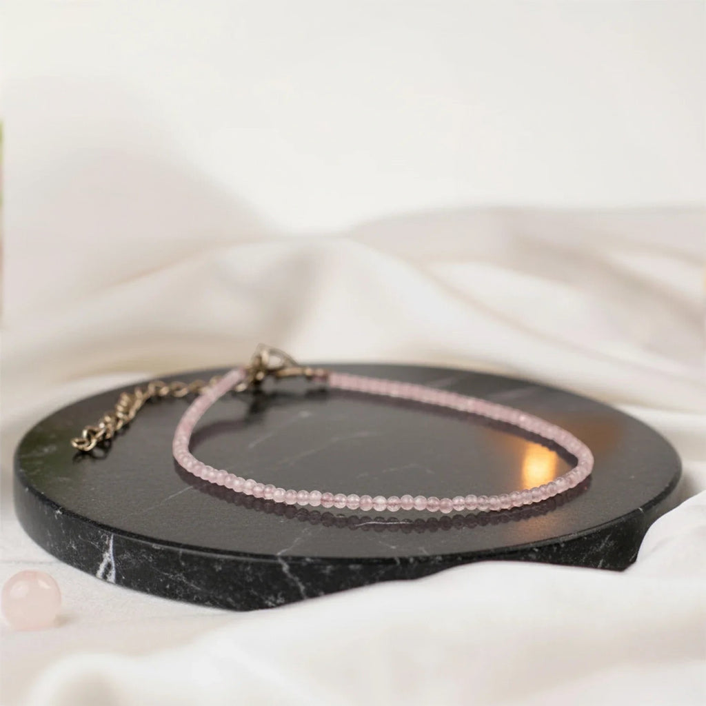 VASTUKOSHA natural rose quartz beaded anklet on a black marble stand with a soft candlelit background.