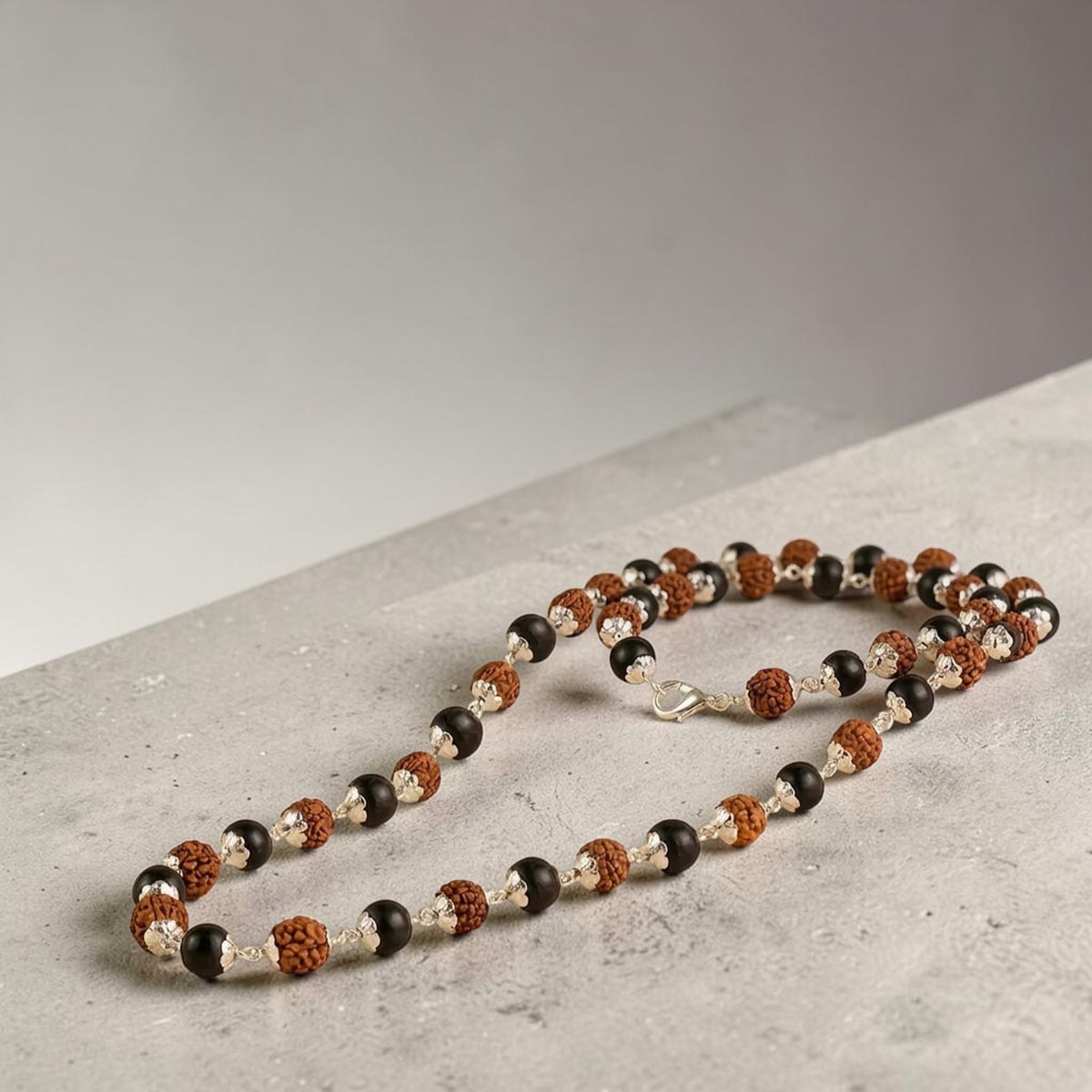 VASTUKOSHA Rishikesh Siddh Rudraksha and Karungali mala with silver capping on a white cloth with flower petals