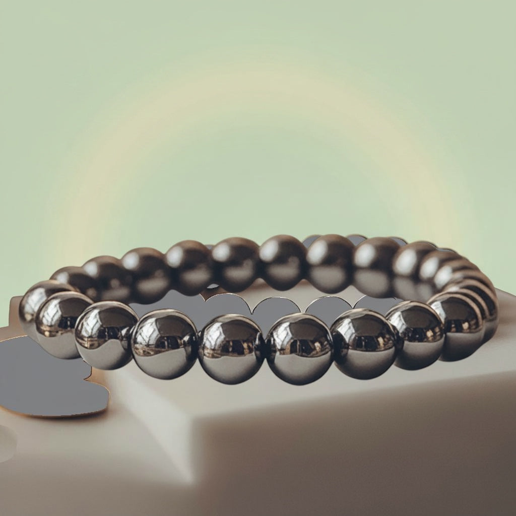 VASTUKOSHA Rinn Mukti bracelet made of polished silver hematite beads resting on a white stone plate with gold coins.