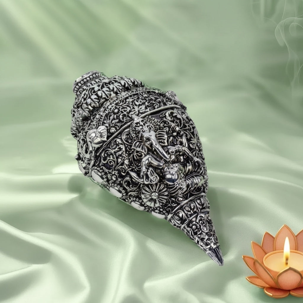 VASTUKOSHA silver-plated conch shell featuring intricate Lord Ganesha carvings, displayed on a soft green fabric.