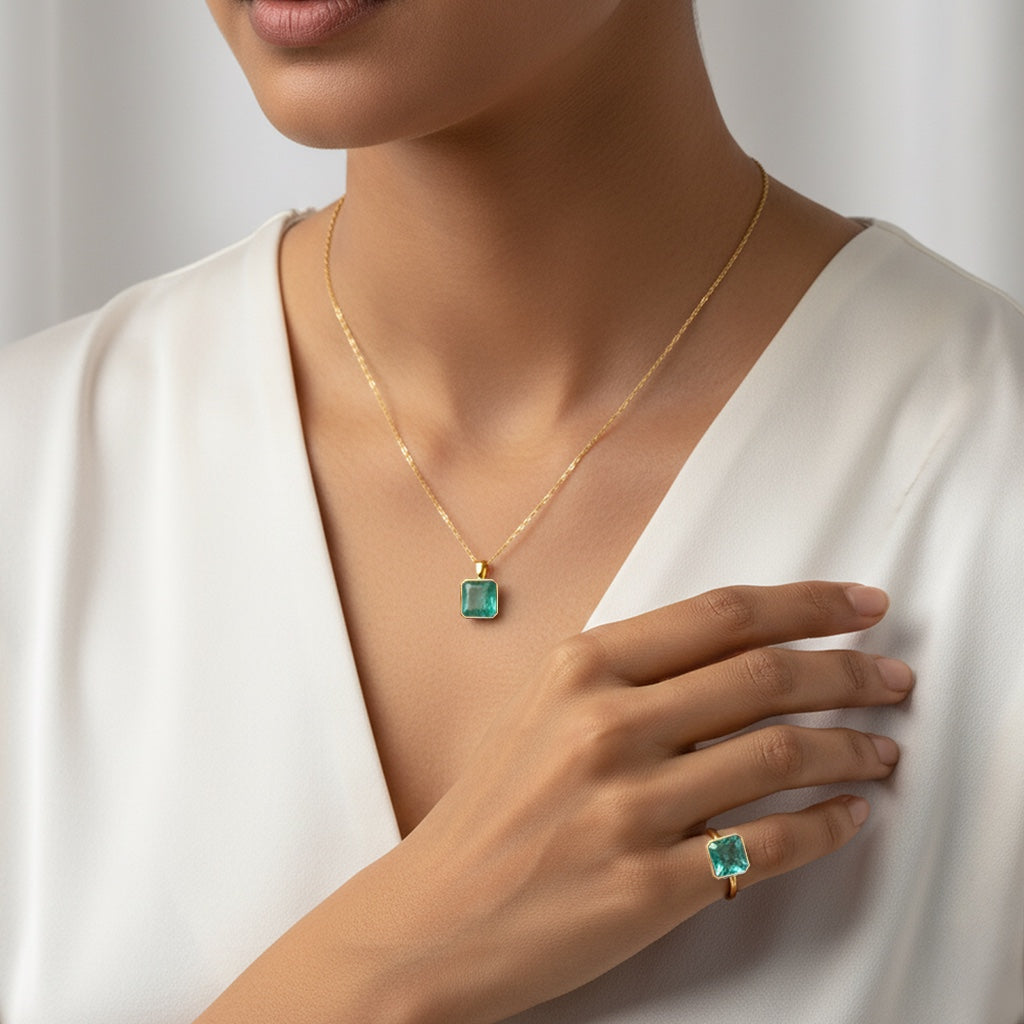 VASTUKOSHA Zambian emerald pendant and ring set in gold, worn by a woman in a white top for a refined look.